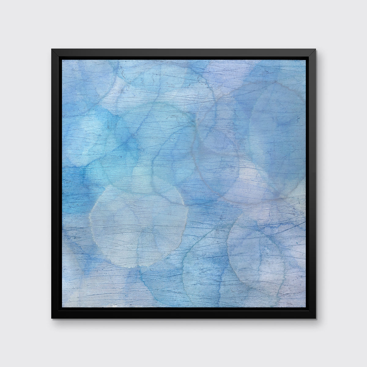 A blue and light blue abstract overlapping circle print in a black floater frame hangs on a white wall.