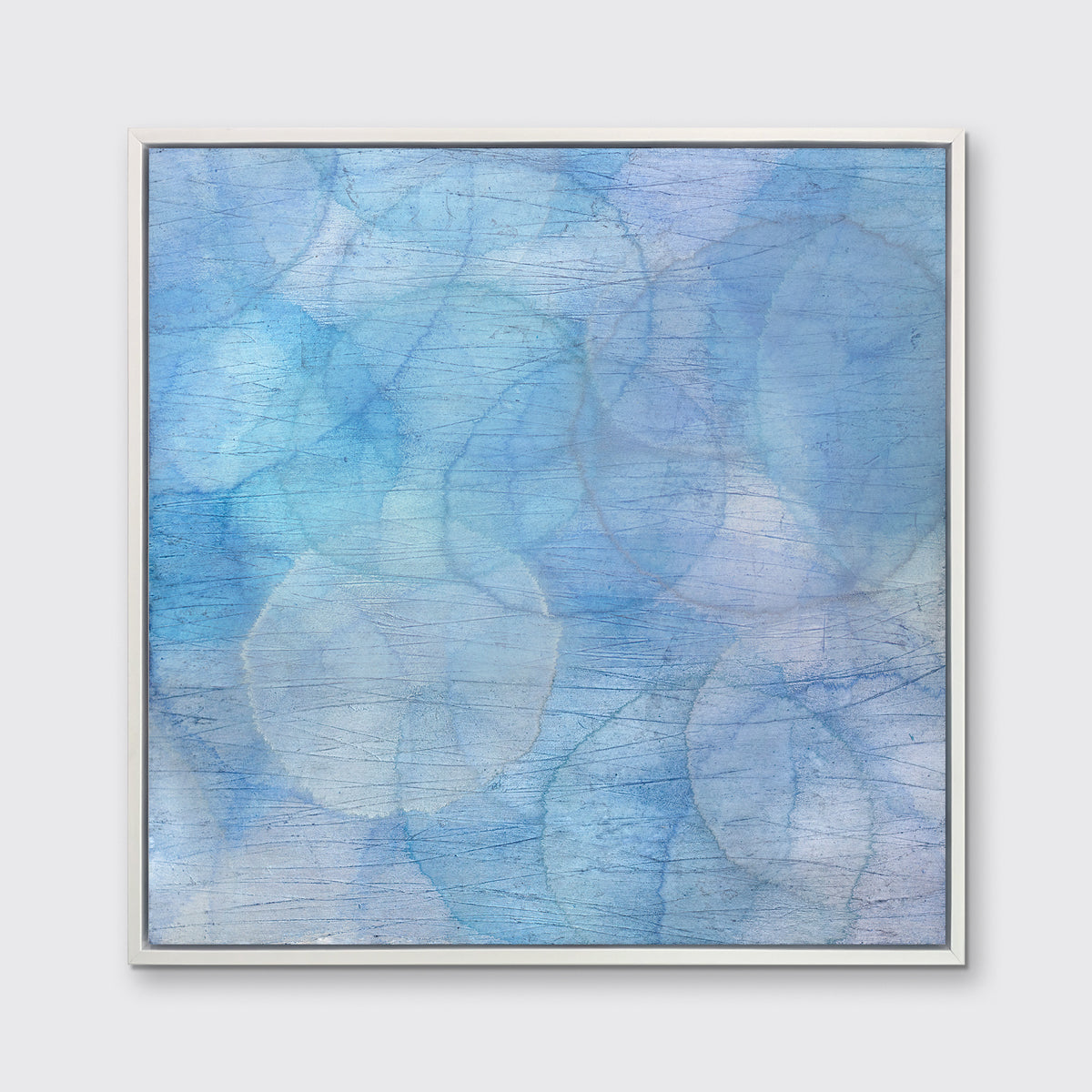A blue and light blue abstract overlapping circle print in a white floater frame hangs on a white wall.