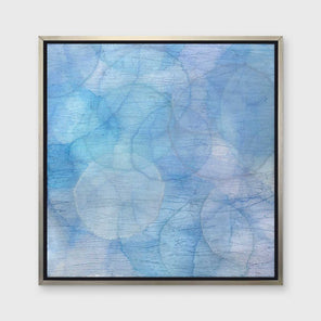 A multiple shades of blue overlapping circles with an iridescence in a silver floater frame hangs on a white wall.