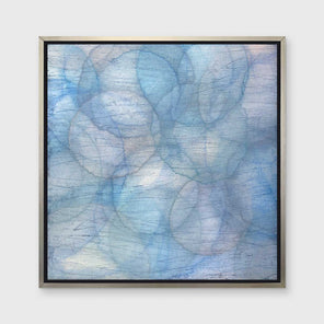 Layers of overlapping circles with an iridescent feel in blues, light purples and light greens staged in a silver floater frame hangs on a white wall.
