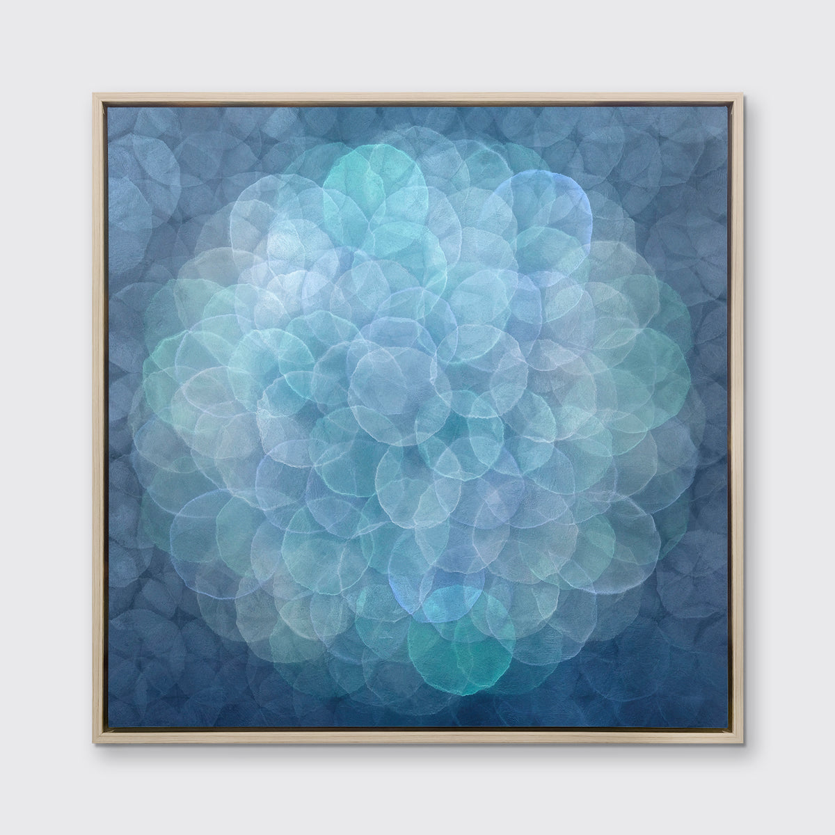 A blue, teal, light lavender and white abstract geometric print in a white oak wood floater frame hangs on a white wall.