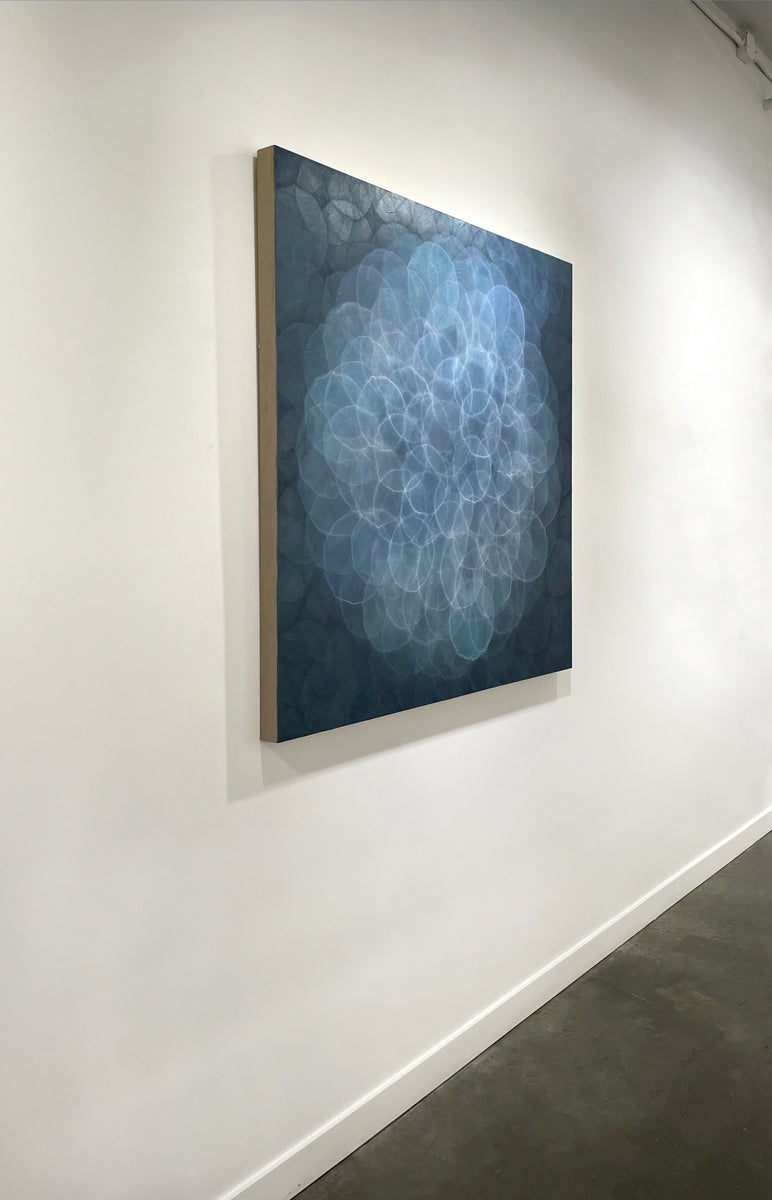 A blue, teal, light lavender and white abstract geometric painting hung on a white wall with a view from the left. 