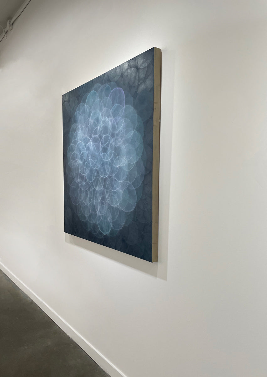 A blue, teal, light lavender and white abstract geometric painting hung on a white wall with a view from the right. 