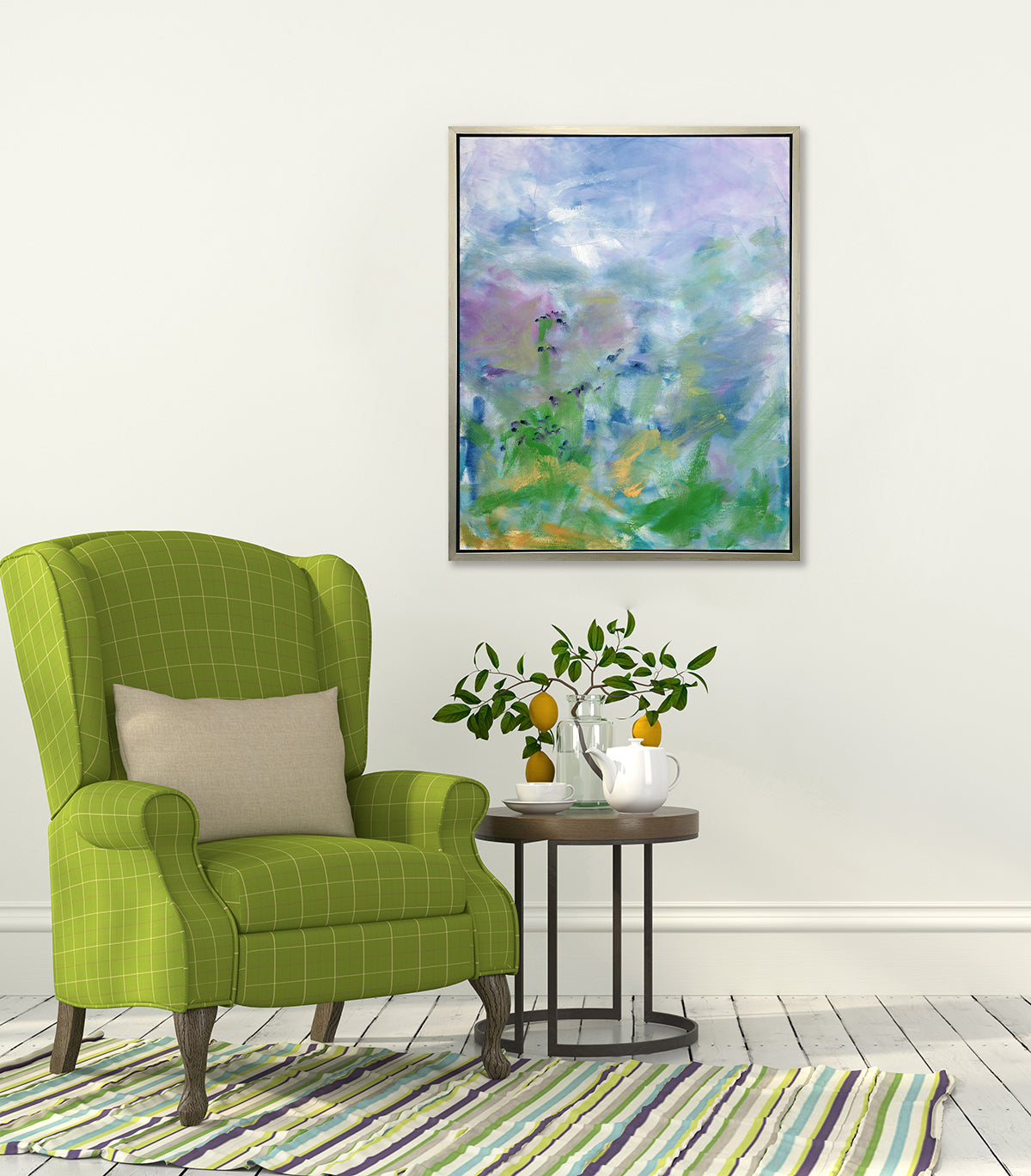 A blue, purple and green abstract print in a silver floater frame hangs on a white wall above a green and white high back chair with an ivory pillow, a round wood side table with a glass vase with a lemon stem and a purple, blue, green and white white striped rug.