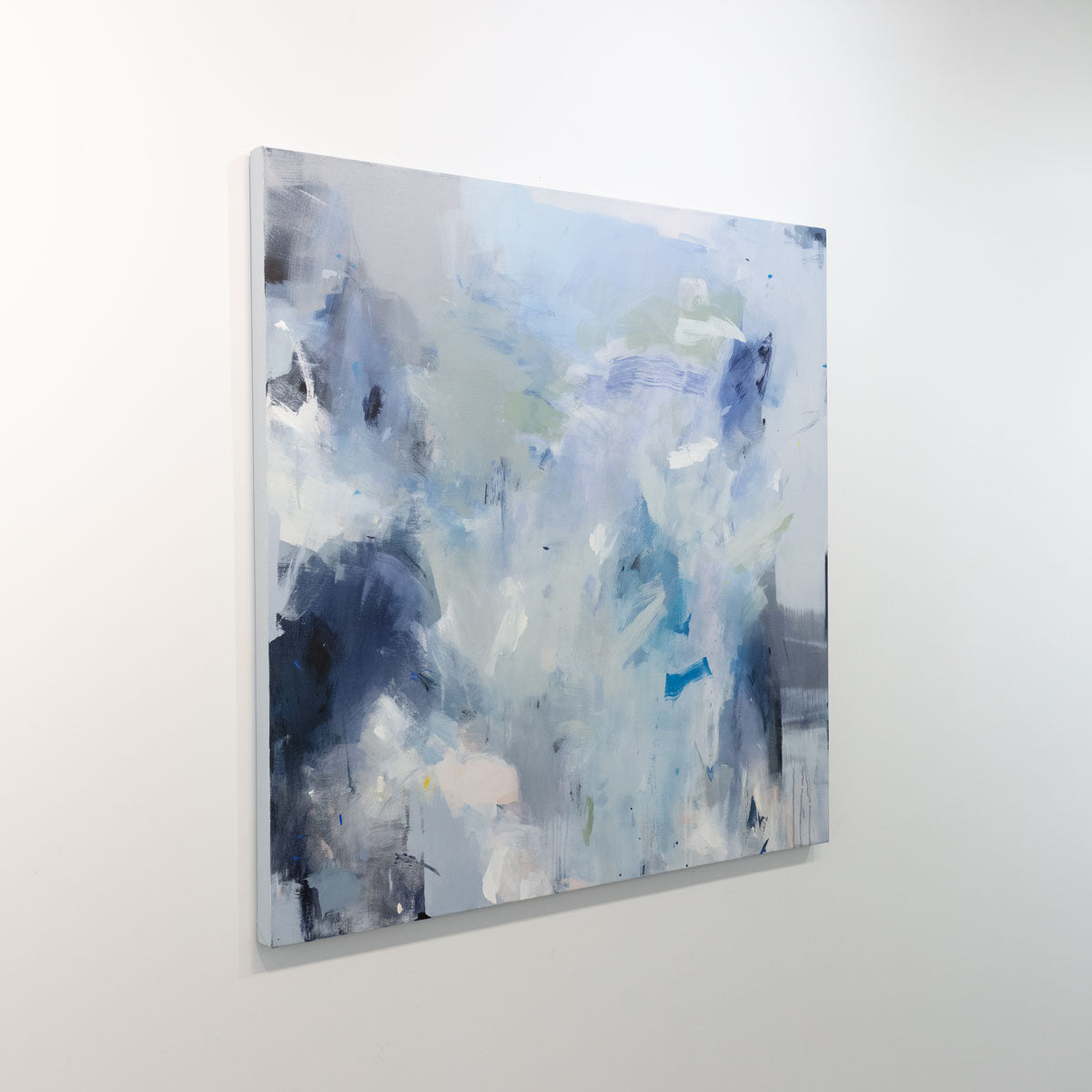 An abstract painting by Kelly Rossetti featuring blue, white and green brushstrokes is seen at an angle on a gallery wall. 
