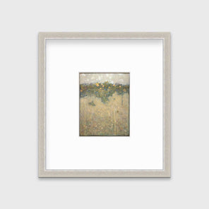 A muted yellow, green and beige abstract landscape print in a silver frame with a mat hangs on a white wall.