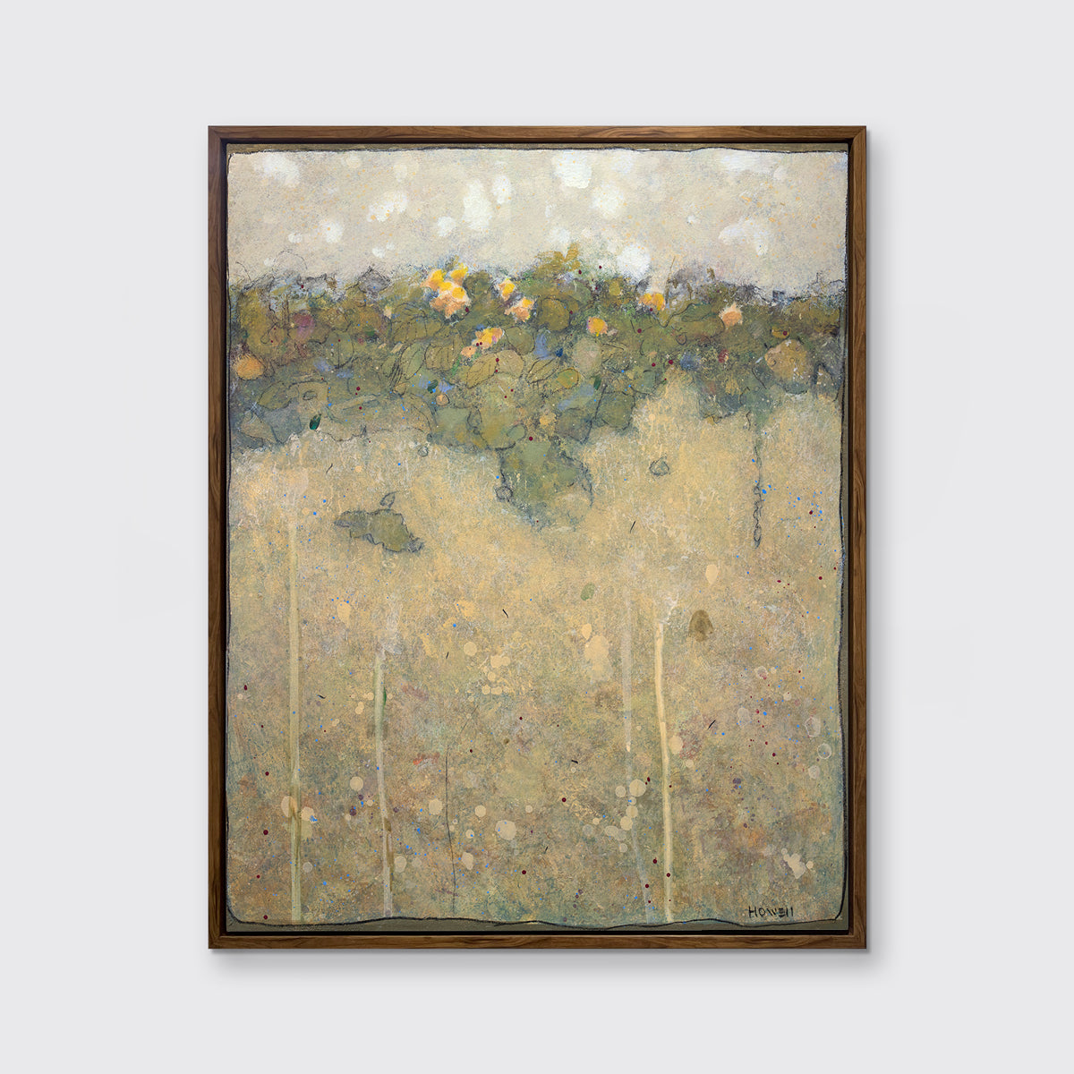 A muted yellow, green and beige abstract landscape print in an oak wood floater frame hangs on a white wall.