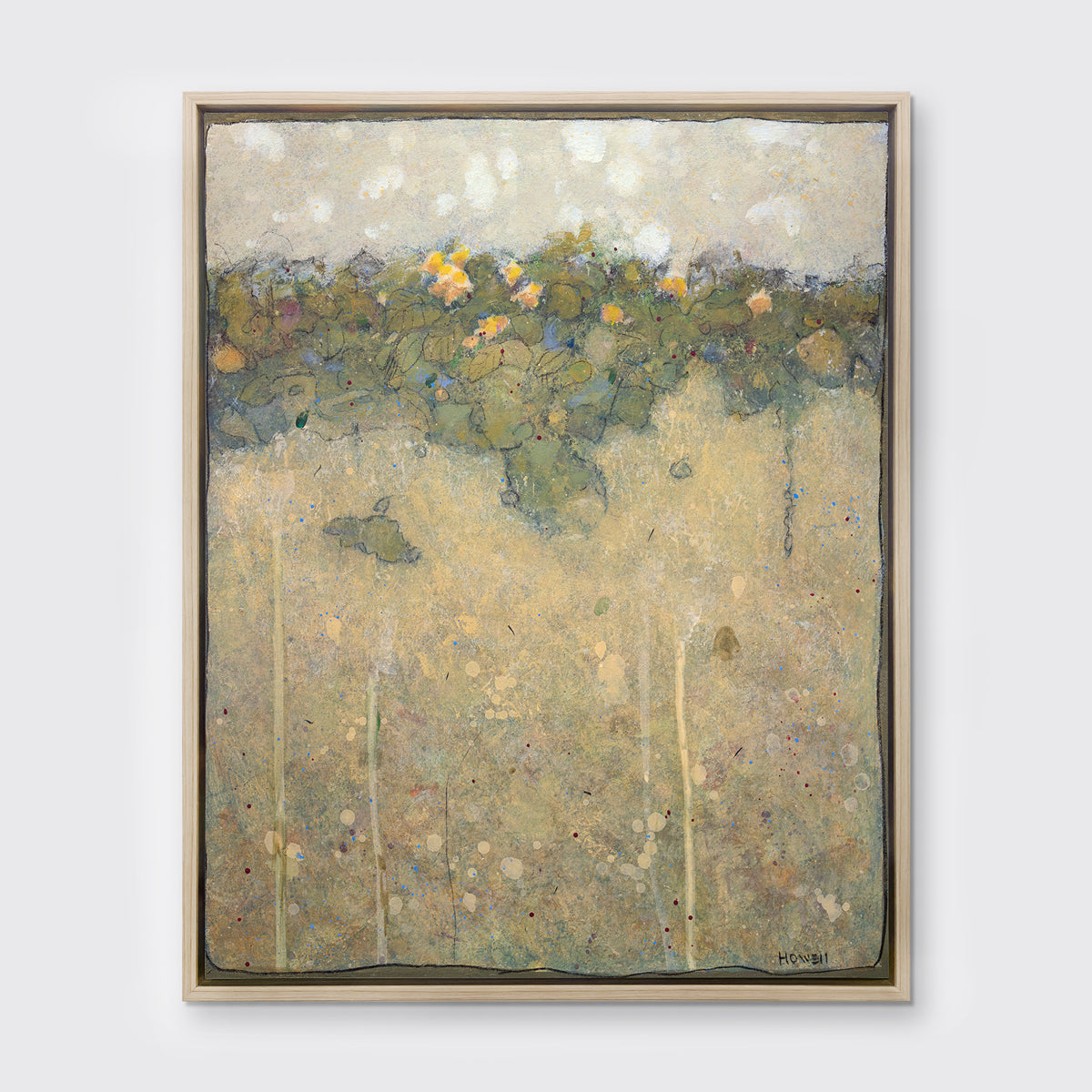 A muted yellow, green and beige abstract landscape print in a white oak wood floater frame hangs on a white wall.