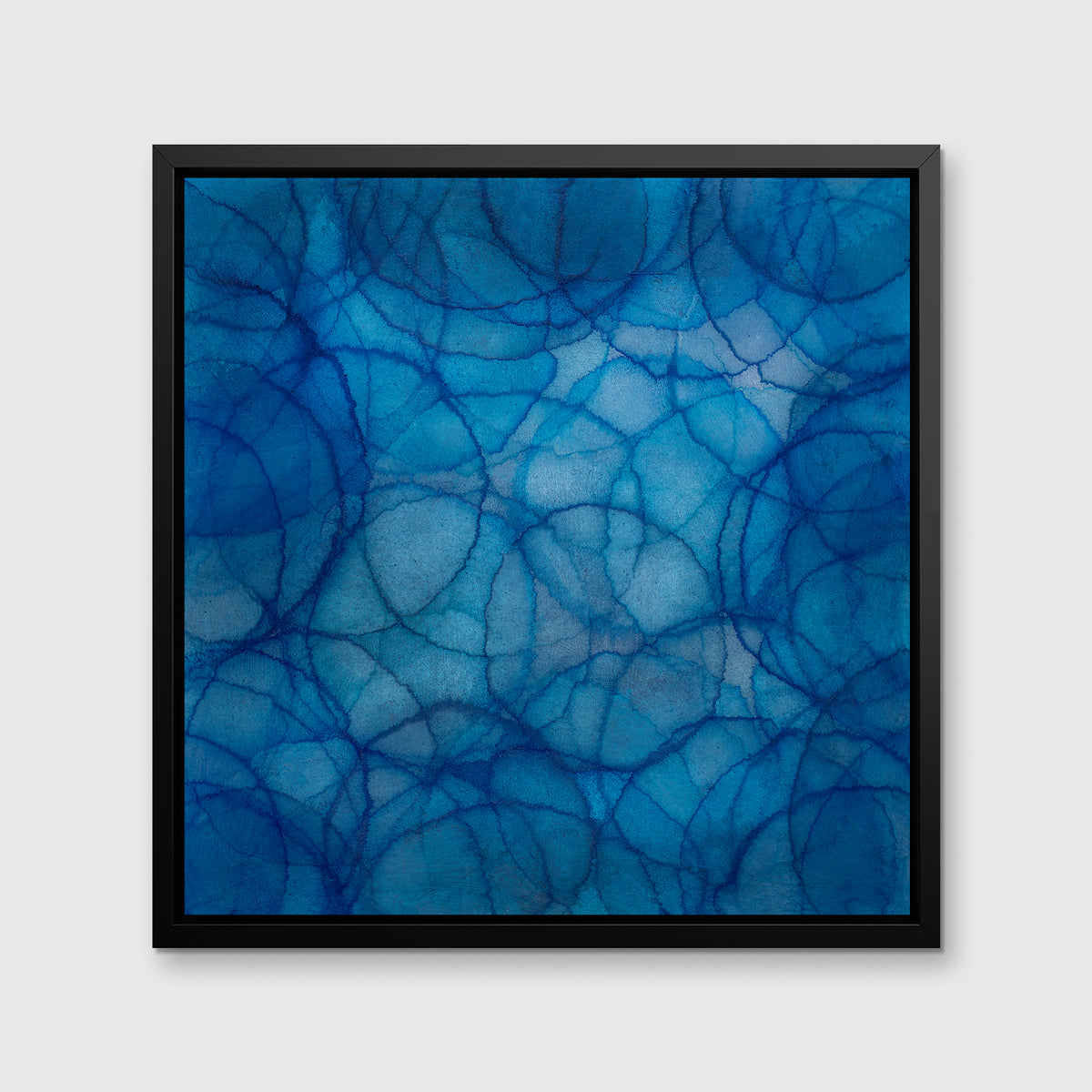 A blue and light blue abstract overlapping circle print in a black floater frame hangs on a white wall.