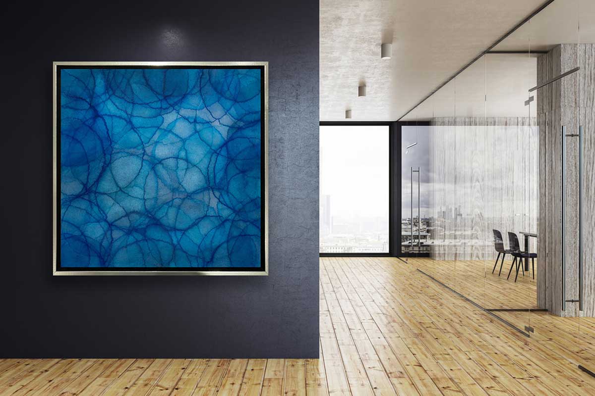 A blue and light blue abstract overlapping circle print in a silver floater frame hangs on a dark navy wall next to a hallway with glass walls and doors leading to offices.