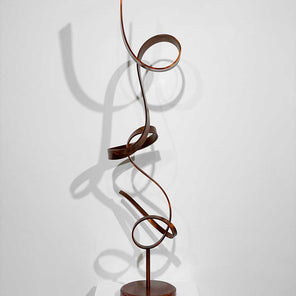 Stainless Steel sculpture with Orange Dye and Clear Coat, from the front view, sitting on a pedestal in front of a white wall.