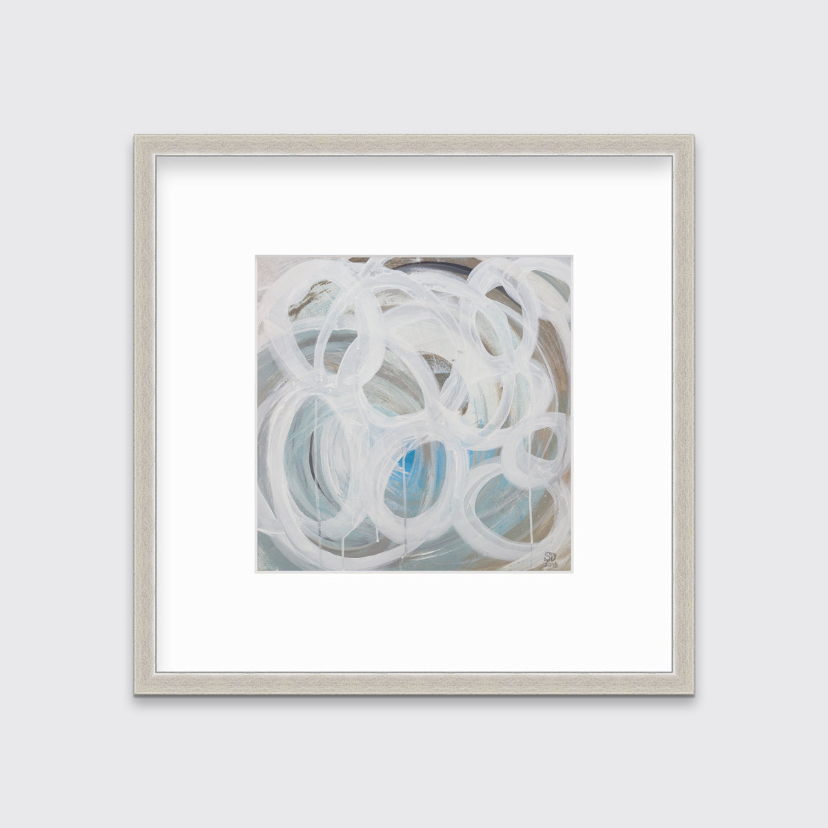 A white, light teal, blue and beige abstract print in a silver frame with a mat hangs on a white wall.