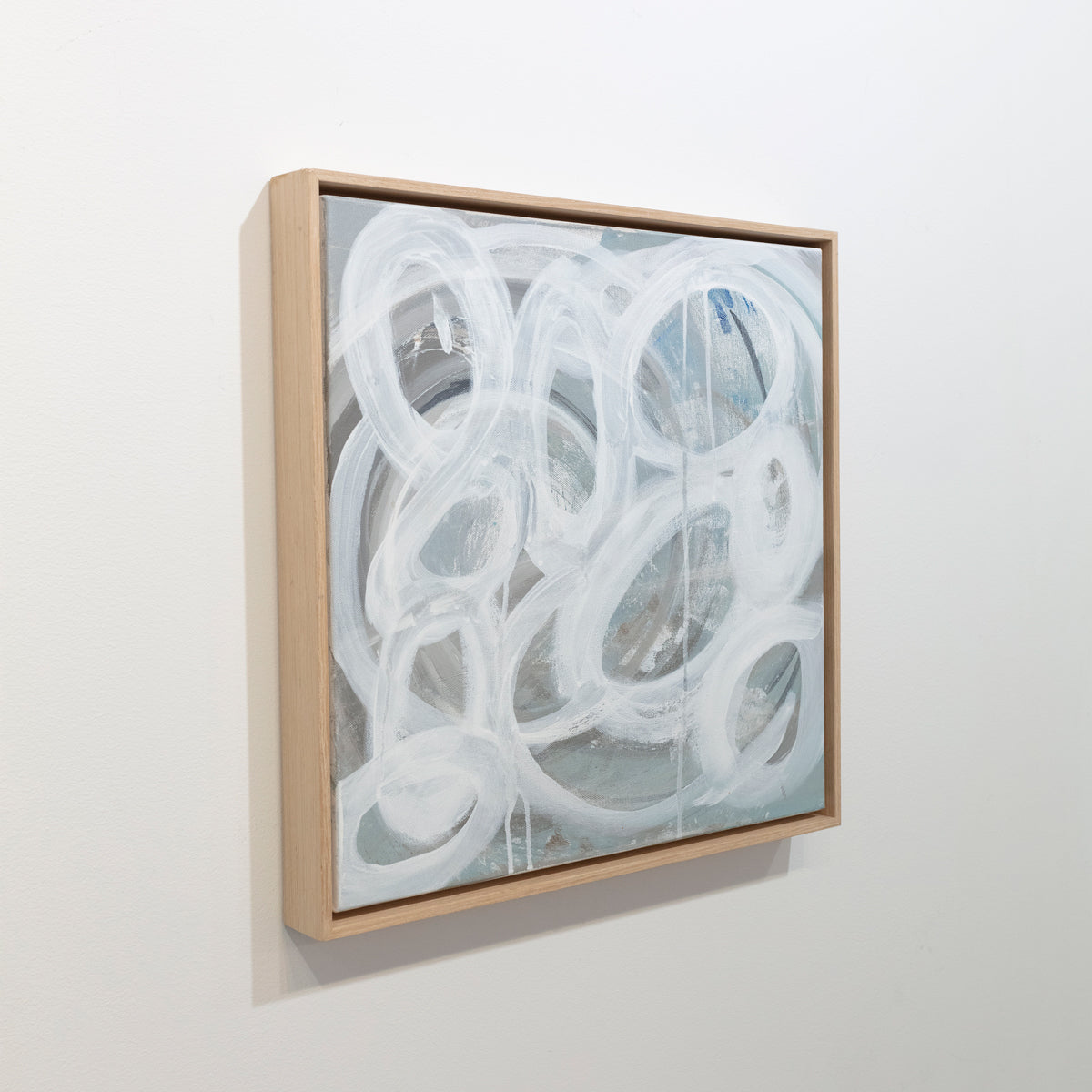 A slate grey canvas painting with white concentric circles is seen at an angle on a gallery wall. Wired and ready to hang.
