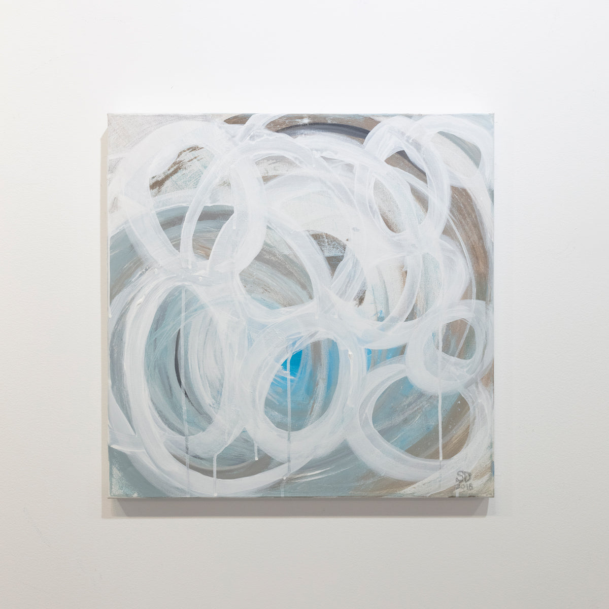 A grey, tan and blue painting with white concentric circles painted on it is hung on a gallery wall. Wired and ready to hang.