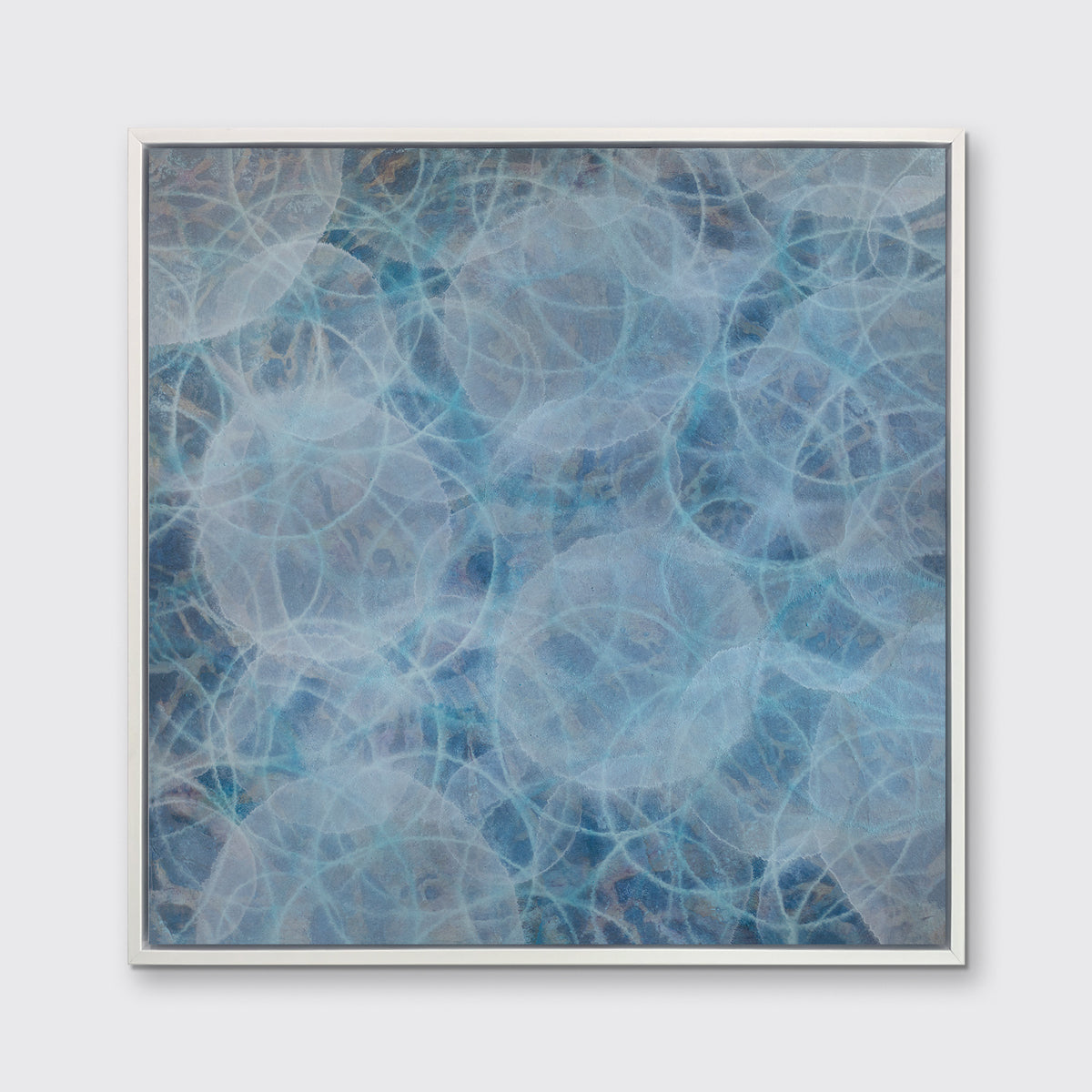A blue, teal and white overlapping circles print in a white floater frame hangs on a white wall.