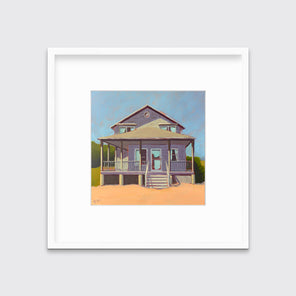 A blue, lavender and peach contemporary beach house print in a white frame with a mat hangs on a white wall.