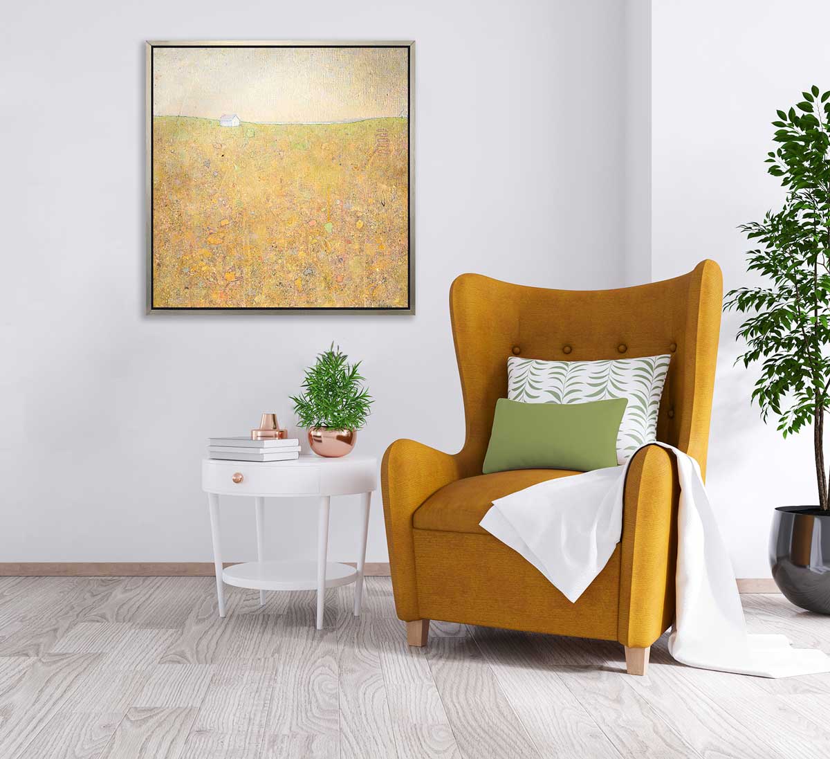 A yellow and grey abstract landscape in a silver floater frame hangs on a grey wall above a dark orange high back chair with green and white pillows, a white throw blanket draped over one side and a white side table with accessories to the left.