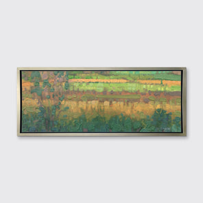 A green, yellow and deep orange abstract landscape print in a silver floater frame hangs on a white wall.