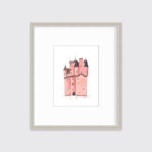 A pink and grey castle print in a silver frame with a mat hangs on a white wall.