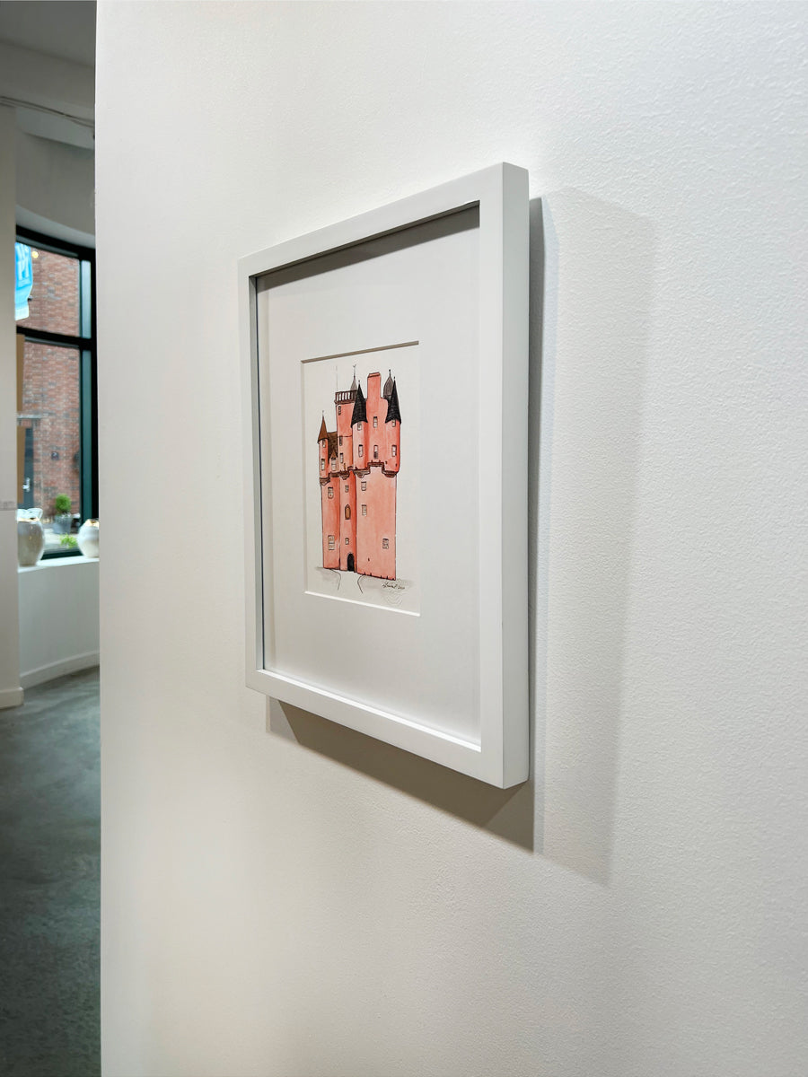 A right side-angle view of a pink, grey and brown illustration drawing of a castle in a white frame with a mat hangs on a white wall. 