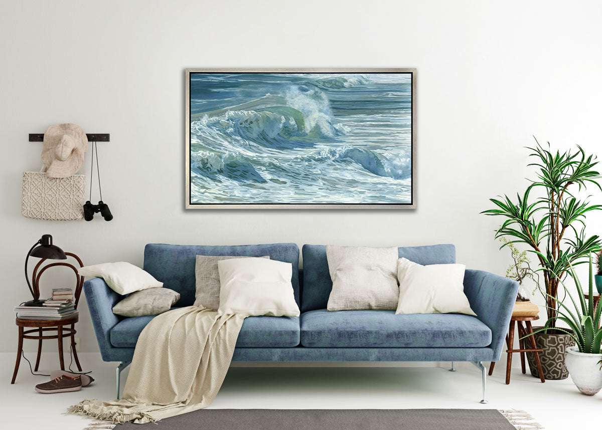 Rolling waves on a side angle with tones of blue, green and white staged in a silver floater frame above a blue sofa.