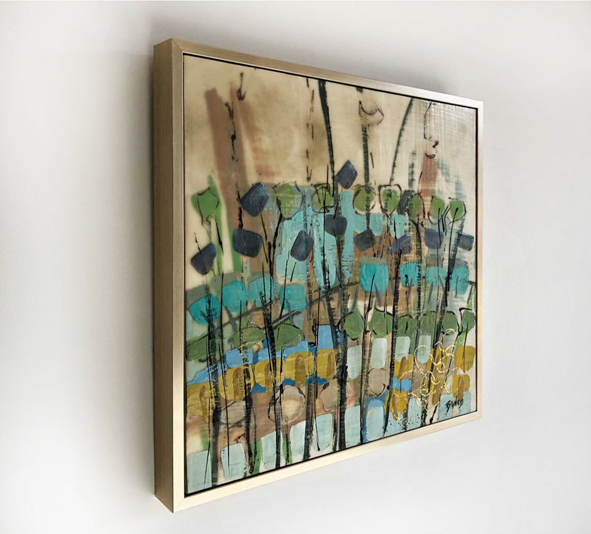 A left-hand side-angle view of an abstract encaustic painting featuring green, blue, and earth tones, and framed in a gold frame hanging on a white wall. 