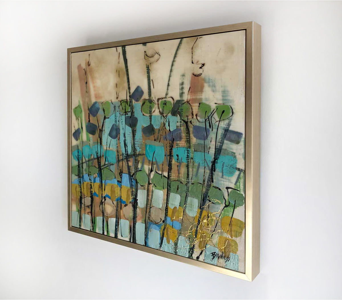 A right-hand side-angle view of an abstract encaustic painting featuring green, blue, and earth tones, and framed in a gold frame hanging on a white wall.