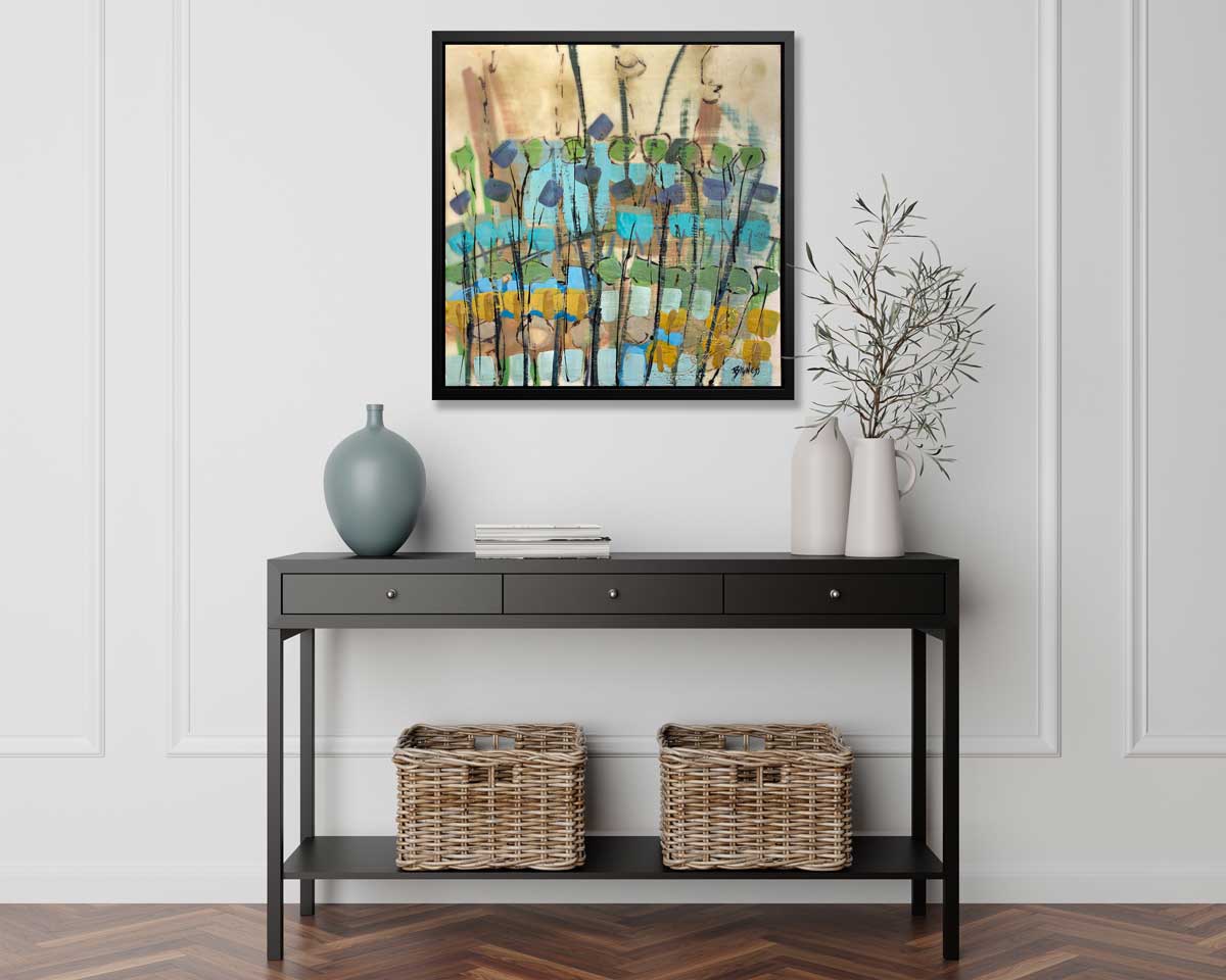 A blue, green, gold and brown abstract floral print in a black frame hangs on a white wall above a black console table with a muted teal vase, two white vases with greenery stems and two wicker baskets.