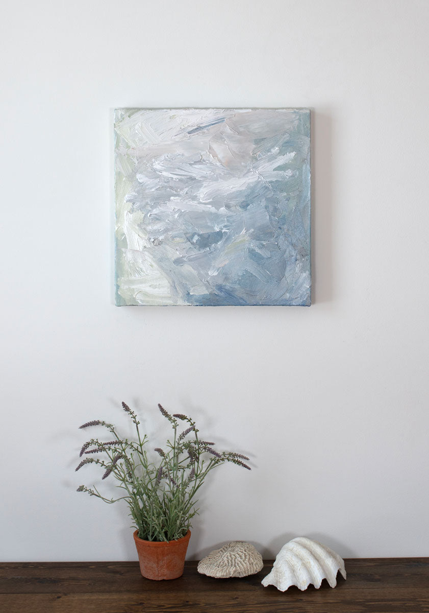A painting is hung above a shelf. It is decorated in white, blue and green paint applied in a thick impasto to its surface. Wired and ready to hang.