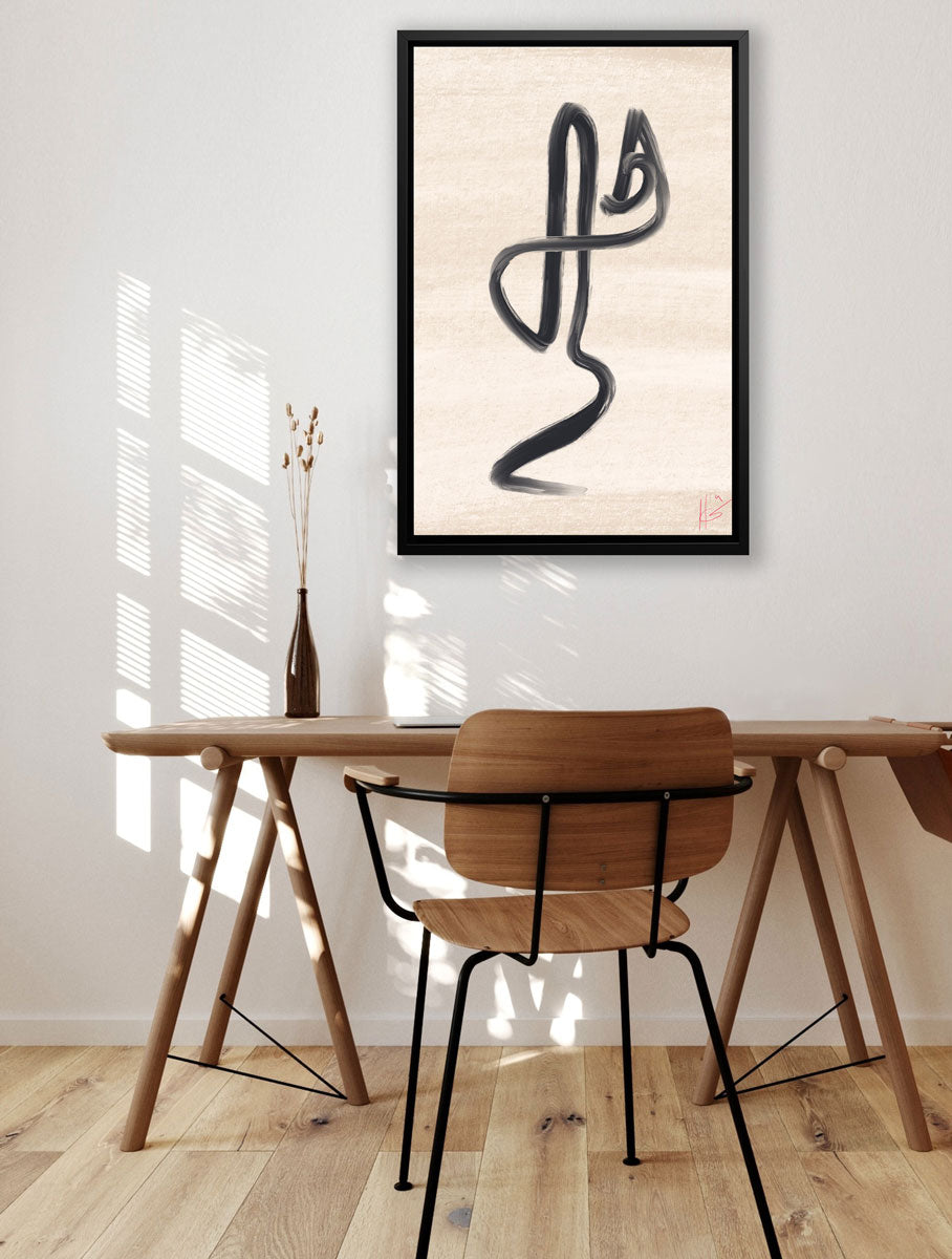 This abstract black and beige art print, framed in a black floater frame, hangs on a white wall above a wood desk and chair. 