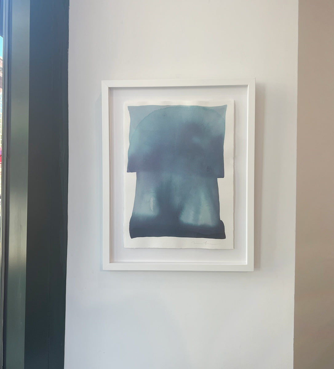 A tonal blue painting with abstract shapes by Nealy Hauschildt in a white frame floating on a white matte on a white wall.