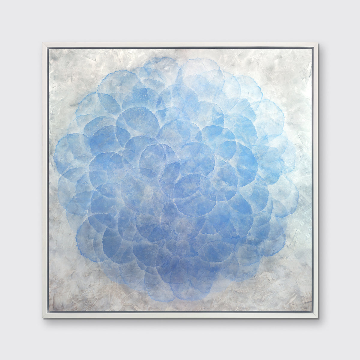 A blue, white and silver abstract geometric print in a white floater frame hangs on a white wall.