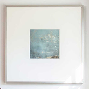 A small light blue and silver painted art mirror in a silver frame with a large white mat hangs on a white wall.