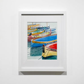 A colorful framed watercolor painting of boats docked in a marina hangs on a white wall. 