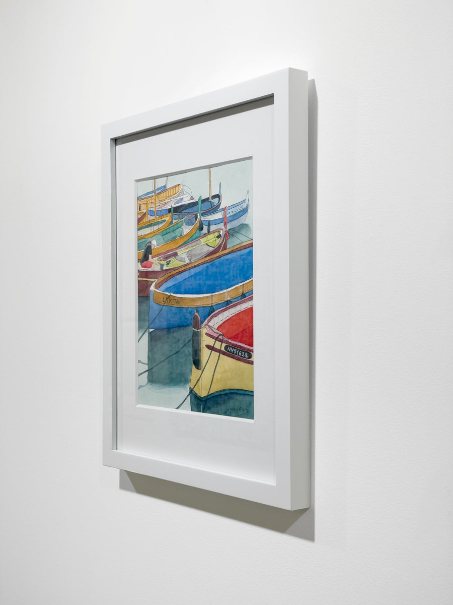 A side view of a colorful framed watercolor painting of boats docked in a marina hanging on a white wall.