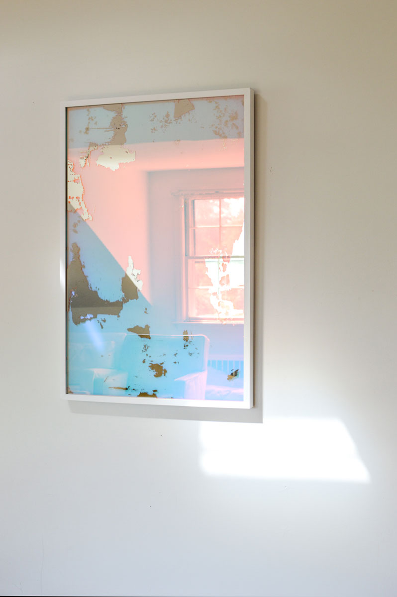 A right side-angle view of an art mirror by Alina B hangs on a white wall.