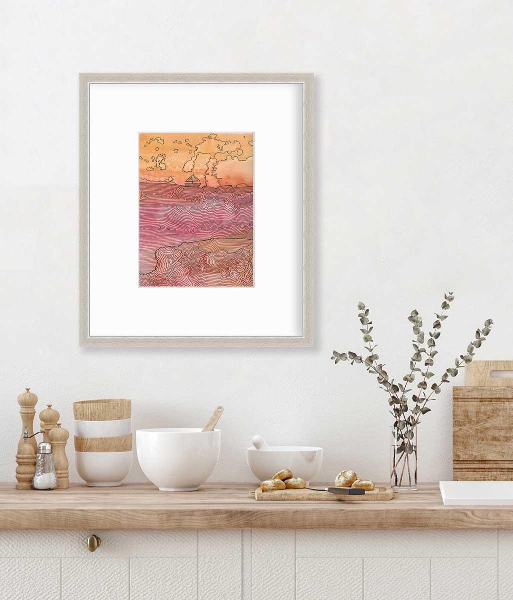 A orange, pink and black abstract landscape with a sailboat in a silver frame with a mat hangs on a white wall above a butcher block countertop with bowls, a cutting board and a clear glass vase with eucalyptus stems.