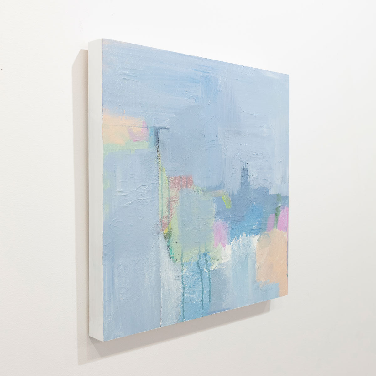 An abstract painting with blue, pink, green and orange patches is seen on a gallery wall at an angle. Wired and ready to hang.