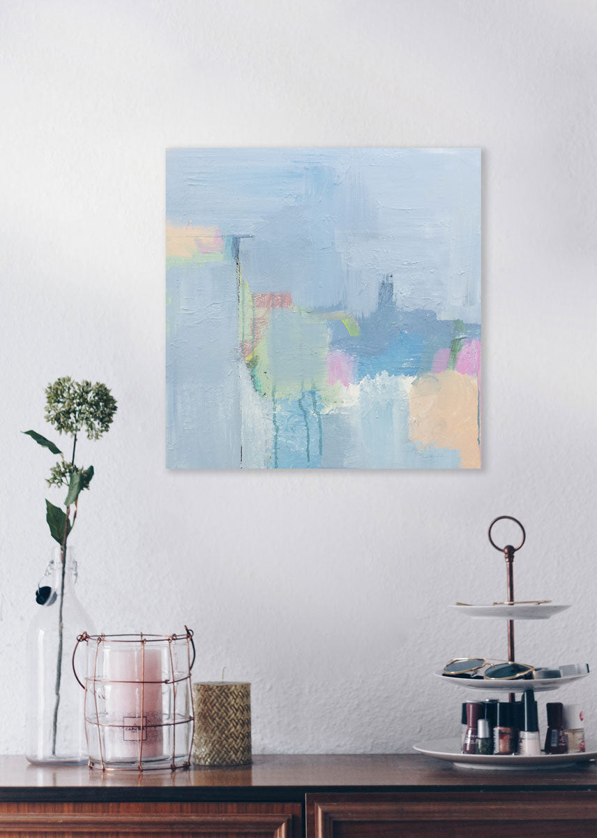 An abstract painting with blue, pink, green and orange patches is hung above various items on a desk. Wired and ready to hang.