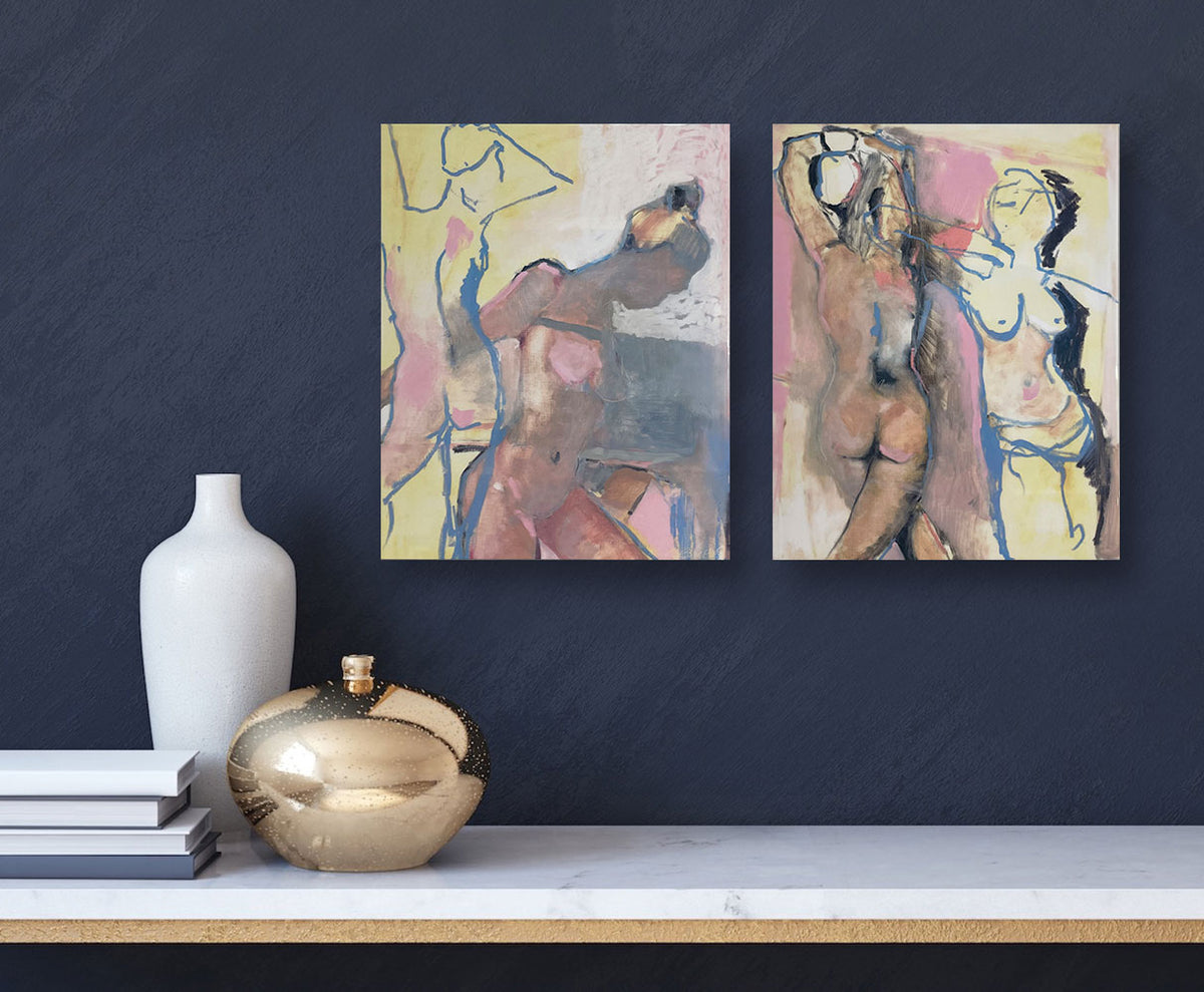 Two pink and yellow abstract nude figurative prints hang on a navy blue wall above a marble console table and modern, white and gold decor vases. 