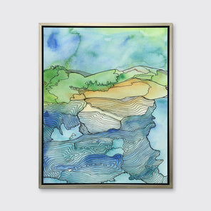 A blue and green landscape illustration canvas print framed in a warm silver frame hangs on a grey wall.