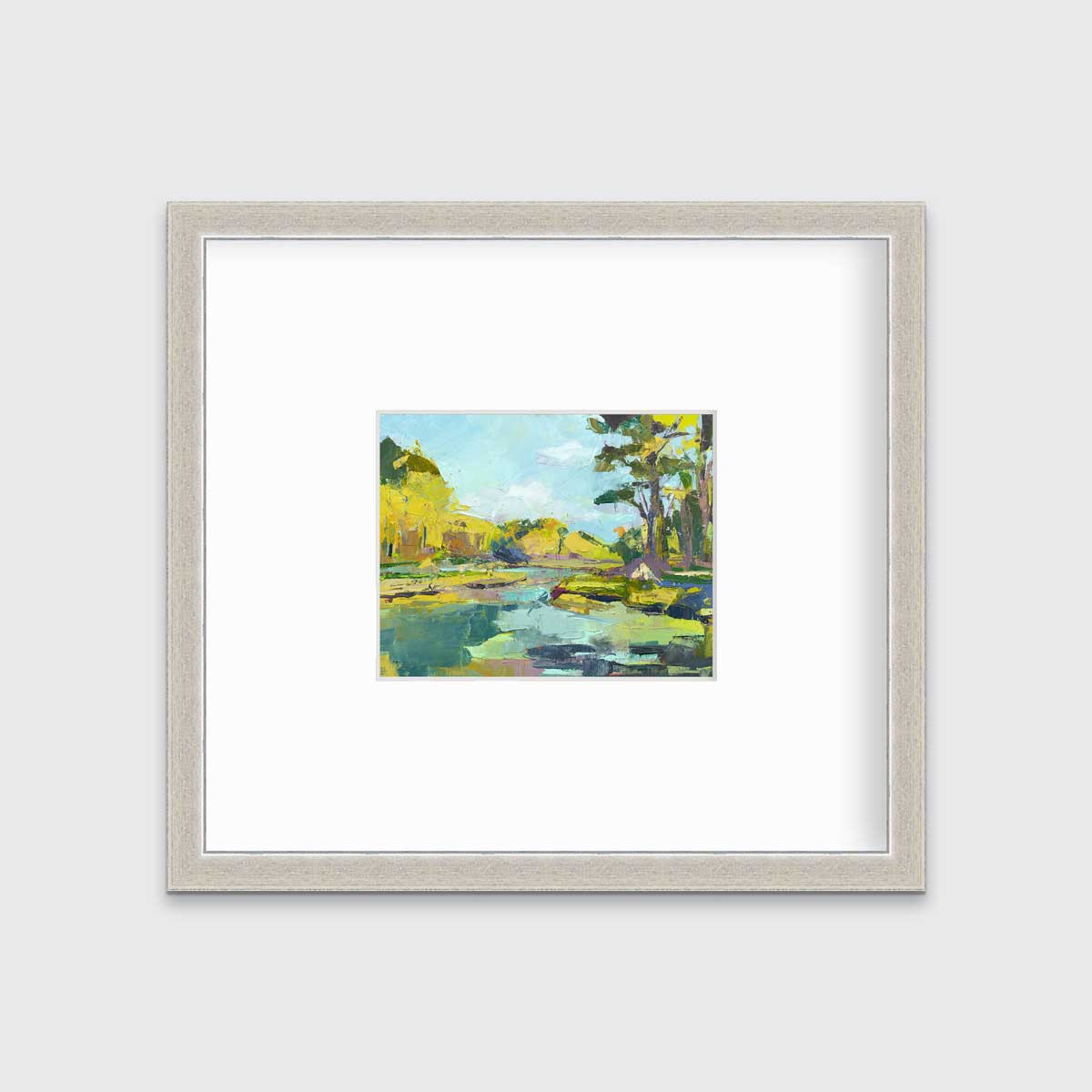 A chartreuse, light blue and green abstract landscape print in a silver frame with a mat hangs on a white wall.
