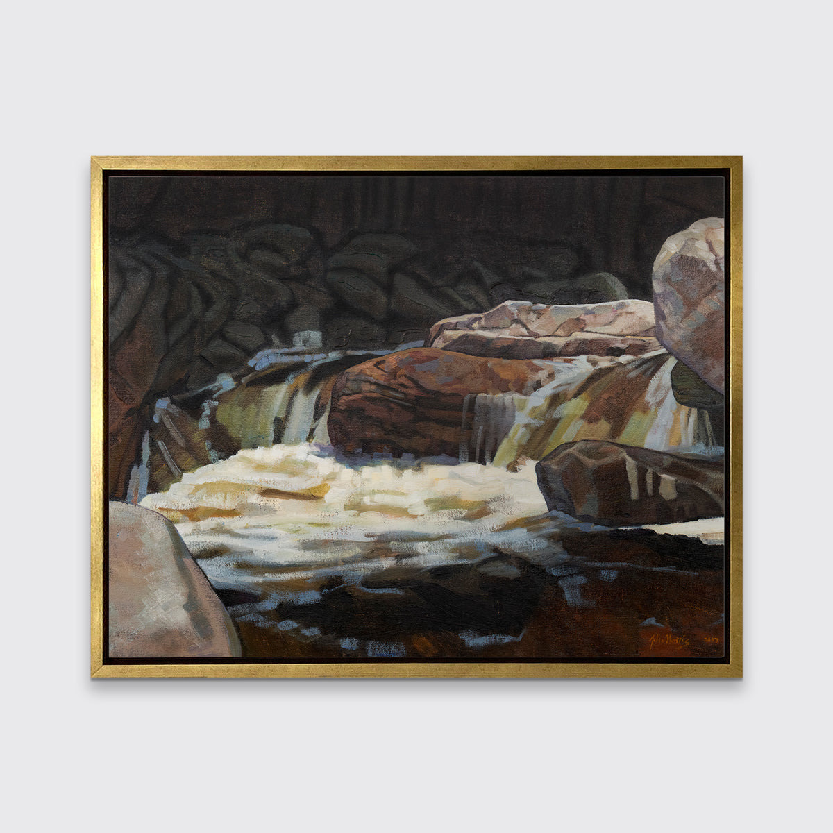 A brown, black and white abstract river landscape print in a gold floater frame hangs on a white wall.