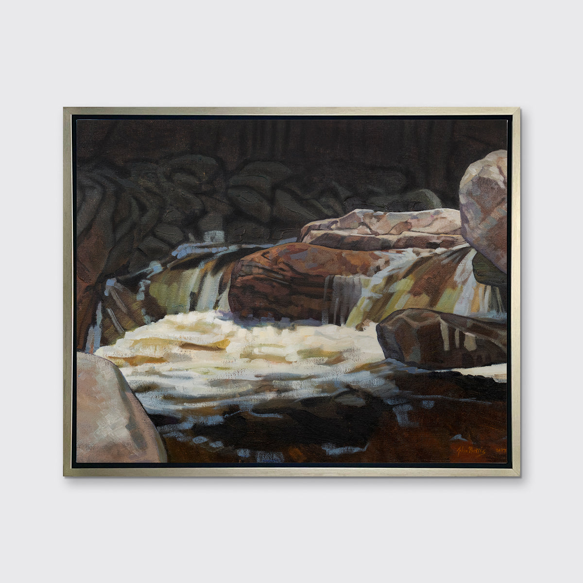 A brown, black and white abstract river landscape print in a silver floater frame hangs on a white wall.