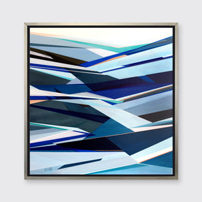 A blue geometric abstract print in a silver floater frame hangs on a white wall.