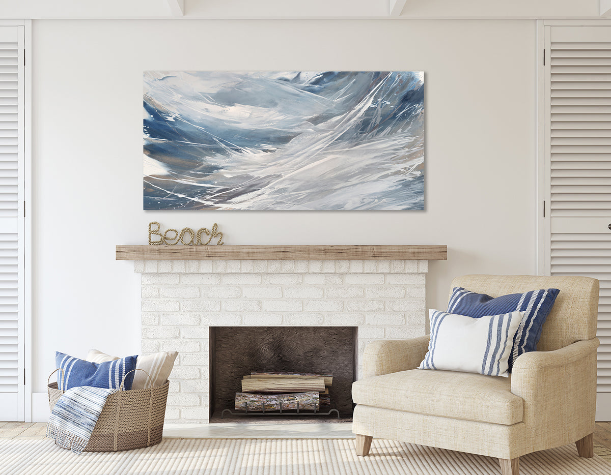 A white, blue, and grey abstract painting by Teodora Guererra hangs on a white wall above a fireplace.  The word BEACH is made as a sculpture in rope sits on the mantel under the painting. A chair apolstered in cream with pillows in blue and white is to the right and a basket with blue and white pillows and a throw sits to the left..