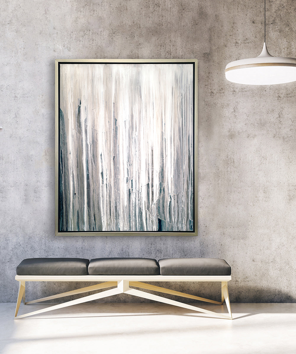 A white, cream and charcoal print in a silver floater frame hangs on a concrete wall above a grey bench.