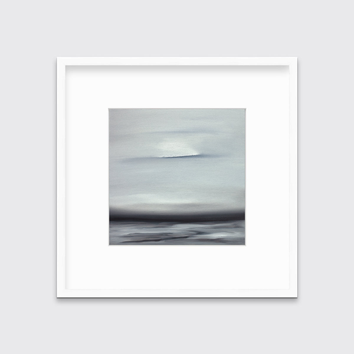 A tonal grey and black print in a white frame with a mat hangs on a white wall.