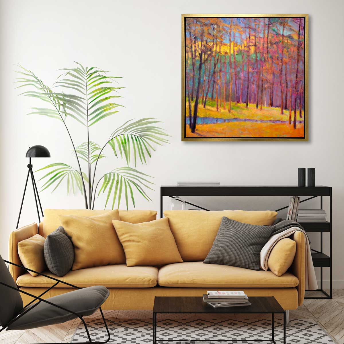 A multicolored abstract tree landscape print in a gold floater frame hangs on a white wall above a black console shelf, a dark yellow sofa with pillows and a small dark wood rectangular coffee table.