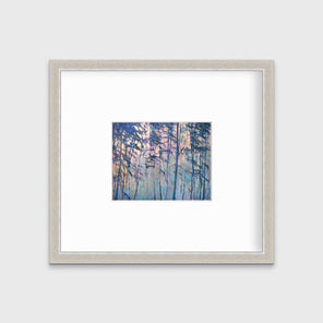 A multicolored abstract tree landscape print in a silver frame with a mat hangs on a white wall.